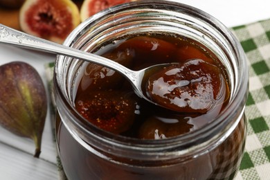 Jar of tasty sweet fig jam on white table, closeup