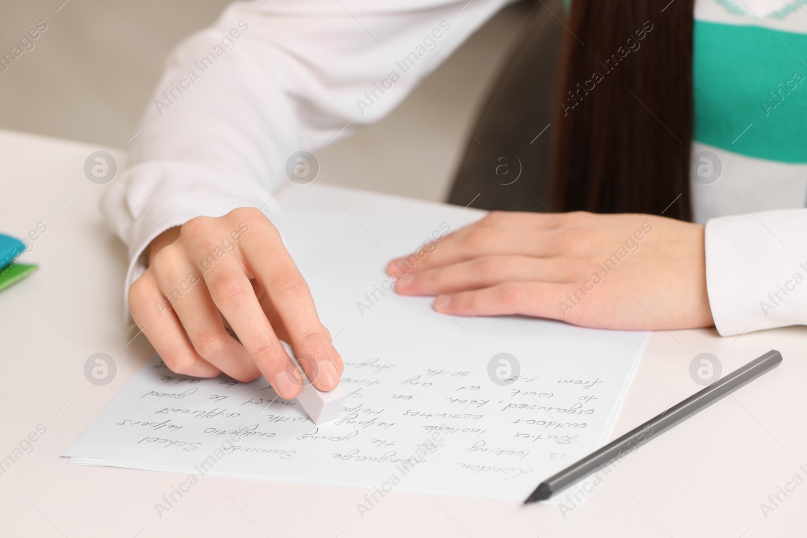 Photo of Girl erasing mistake in her notebook at white desk, closeup