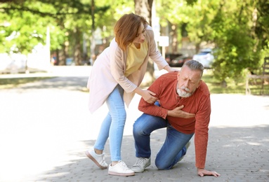 Woman helping mature man suffering from heart attack in park