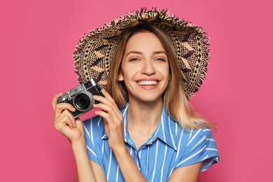 Beautiful young woman with straw hat and camera on crimson background. Stylish headdress