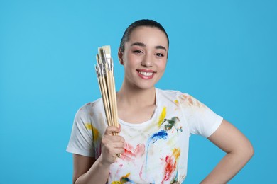 Photo of Woman with paintbrushes on light blue background. Young artist