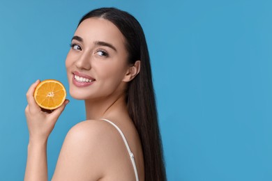 Beautiful young woman with piece of orange on light blue background. Space for text