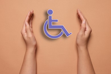 Disability inclusion. Woman protecting wheelchair symbol on coral background, closeup