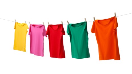 Different bright t-shirts drying on washing line against white background