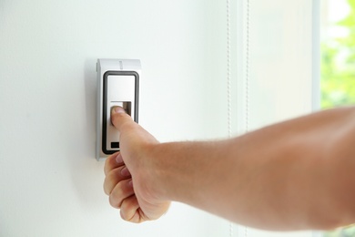 Mature man pressing fingerprint scanner on alarm system indoors