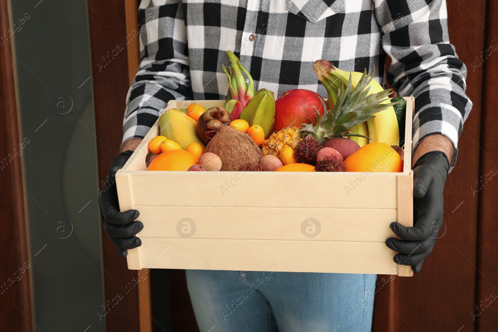 Photo of Courier holding crate with assortment of exotic fruits outdoors, closeup