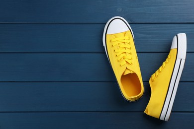 Photo of Pair of yellow sneakers on blue wooden table, flat lay. Space for text