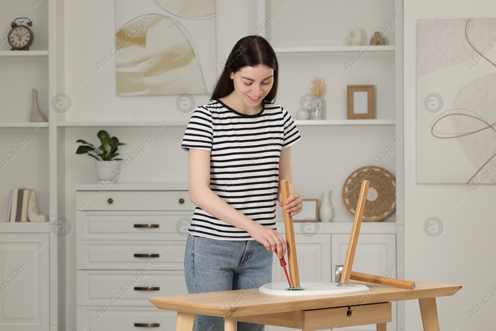 Photo of Young woman with screwdriver assembling furniture at table in room