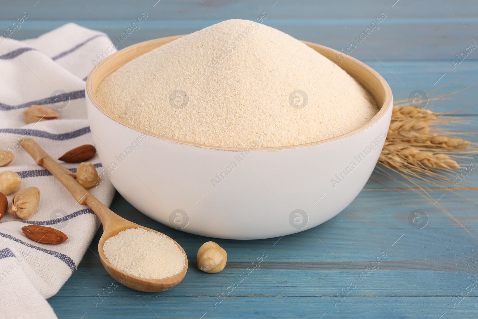 Photo of Uncooked organic semolina, spikelets and different nuts on light blue wooden table