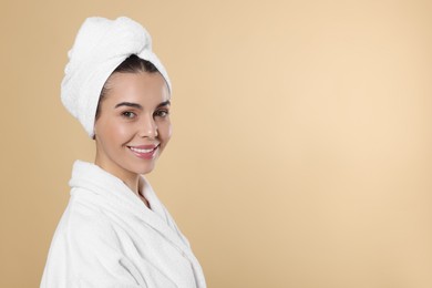 Photo of Young woman in bathrobe with towel on beige background, space for text. Spa treatment