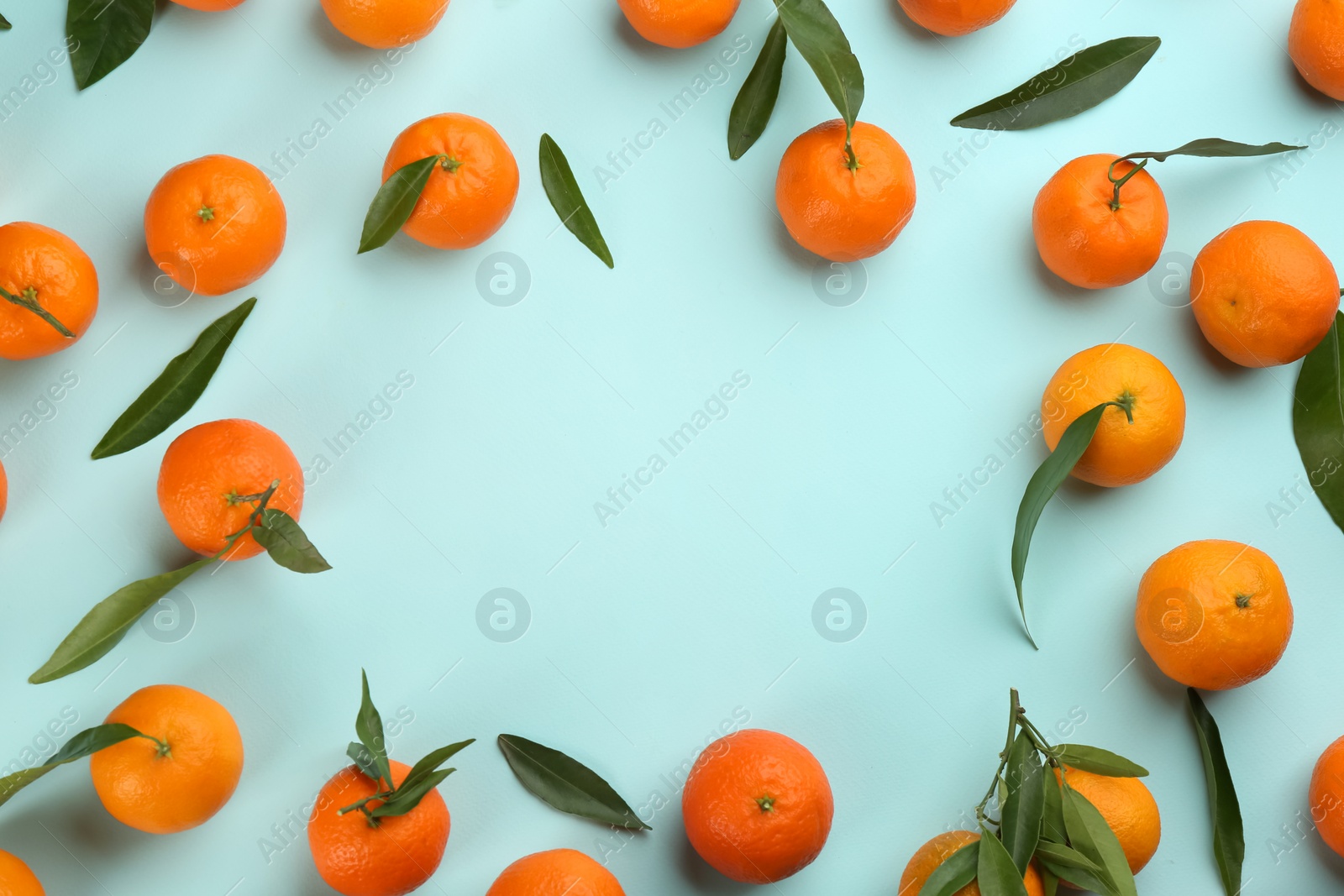 Photo of Frame made of fresh tangerines with green leaves on light blue background, flat lay. Space for text