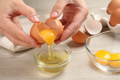 Woman separating egg yolk from white over glass bowl at wooden table, closeup