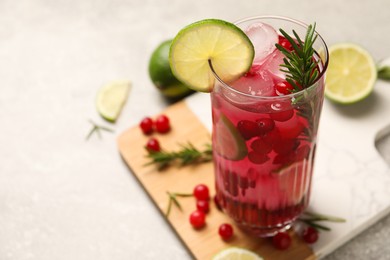 Photo of Tasty cranberry cocktail with rosemary and lime in glass on gray table, closeup. Space for text