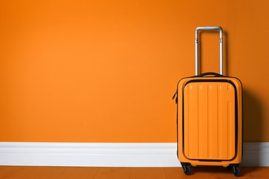 Bright suitcase near orange wall. Space for text