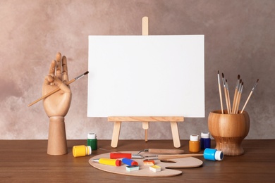 Photo of Wooden easel with blank canvas board and painting tools for children on table near color wall