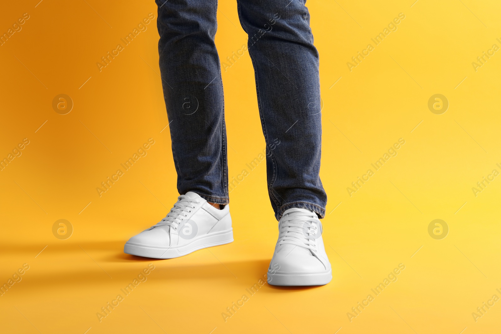 Photo of Man wearing stylish white sneakers on yellow background, closeup