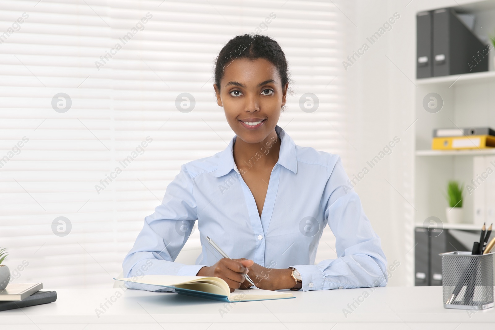 Photo of Smiling African American intern working at white table in office