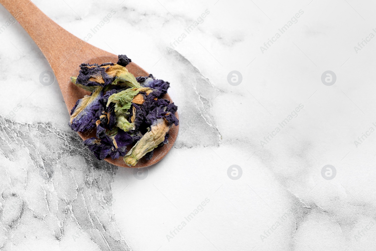 Photo of Spoon of dry organic blue Anchan on white marble table, top view with space for text. Herbal tea