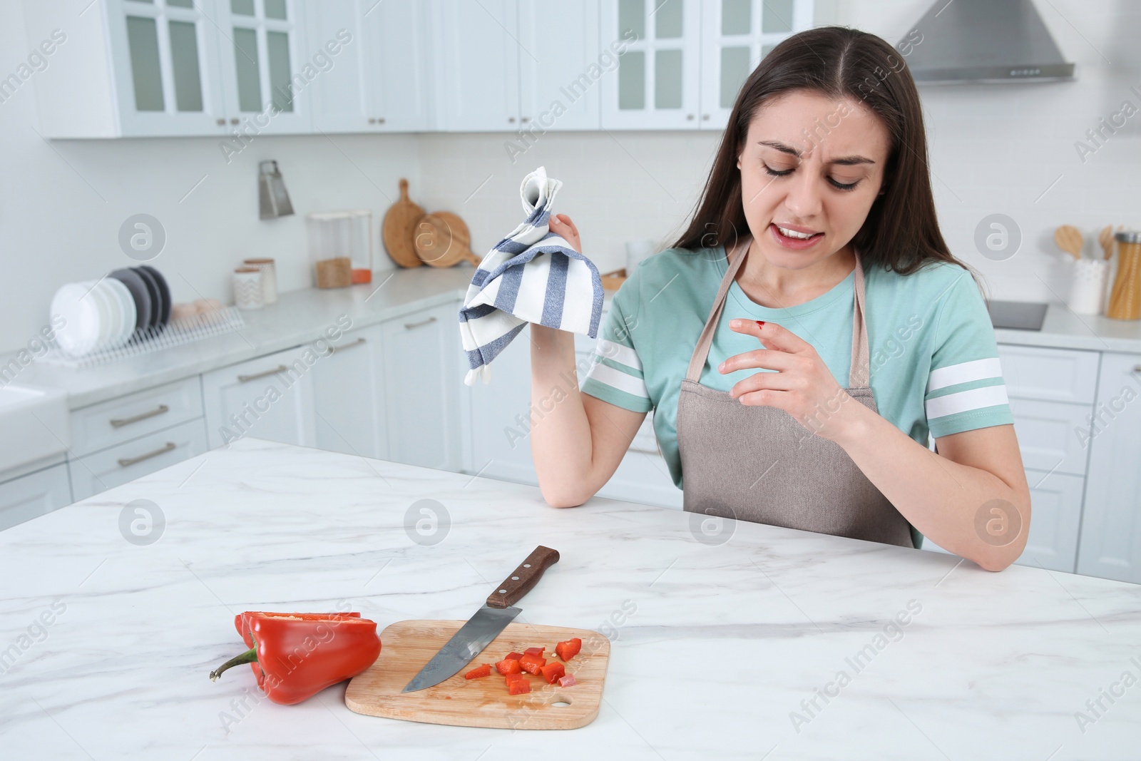 Photo of Woman cut finger with knife while cooking in kitchen