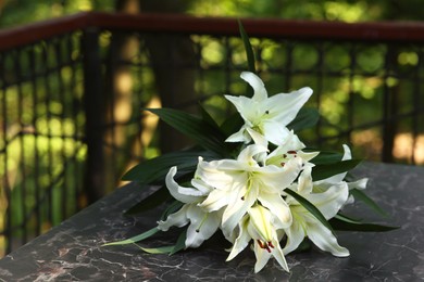 Photo of White lilies on tombstone at cemetery outdoors. Funeral ceremony