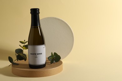 Bottle of delicious white wine and eucalyptus branches on beige background, space for text