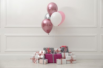Many gift boxes and balloons near white wall