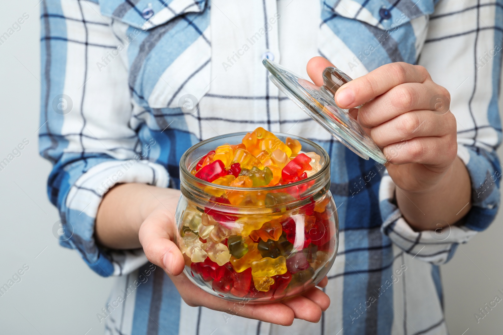 Photo of Woman holding jar of colorful jelly bears on light background, closeup