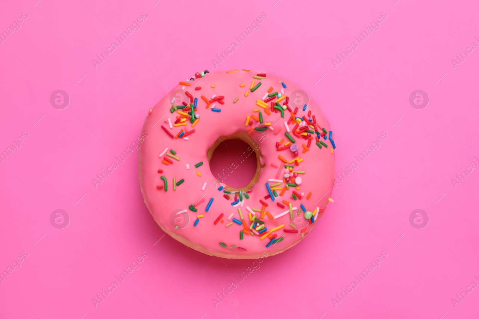 Photo of Sweet glazed donut decorated with sprinkles on pink background, top view. Tasty confectionery