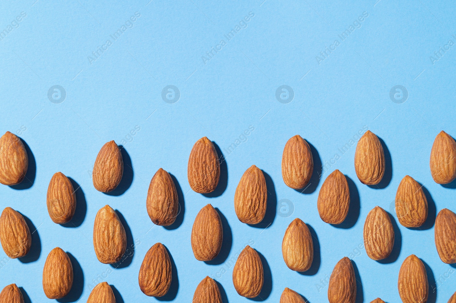 Photo of Delicious raw almonds on light blue background, flat lay. Space for text