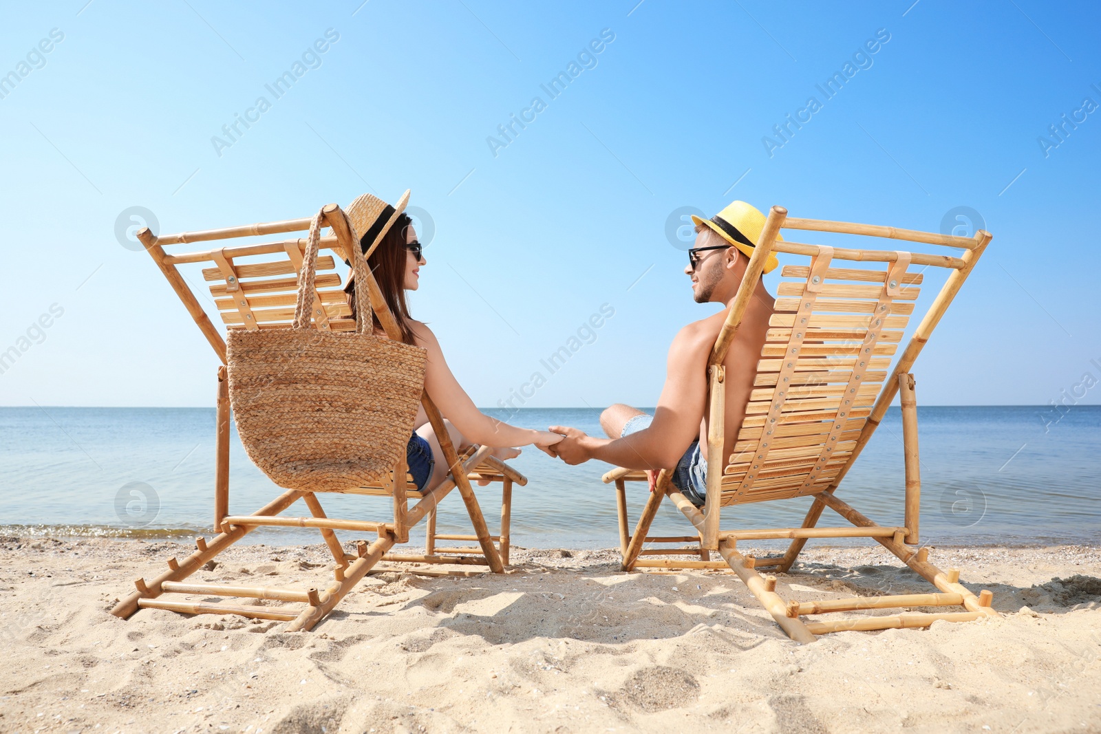 Photo of Young couple relaxing in deck chairs on beach