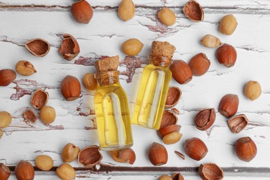 Photo of Bottles of hazelnut essential oil and nuts on wooden table, flat lay