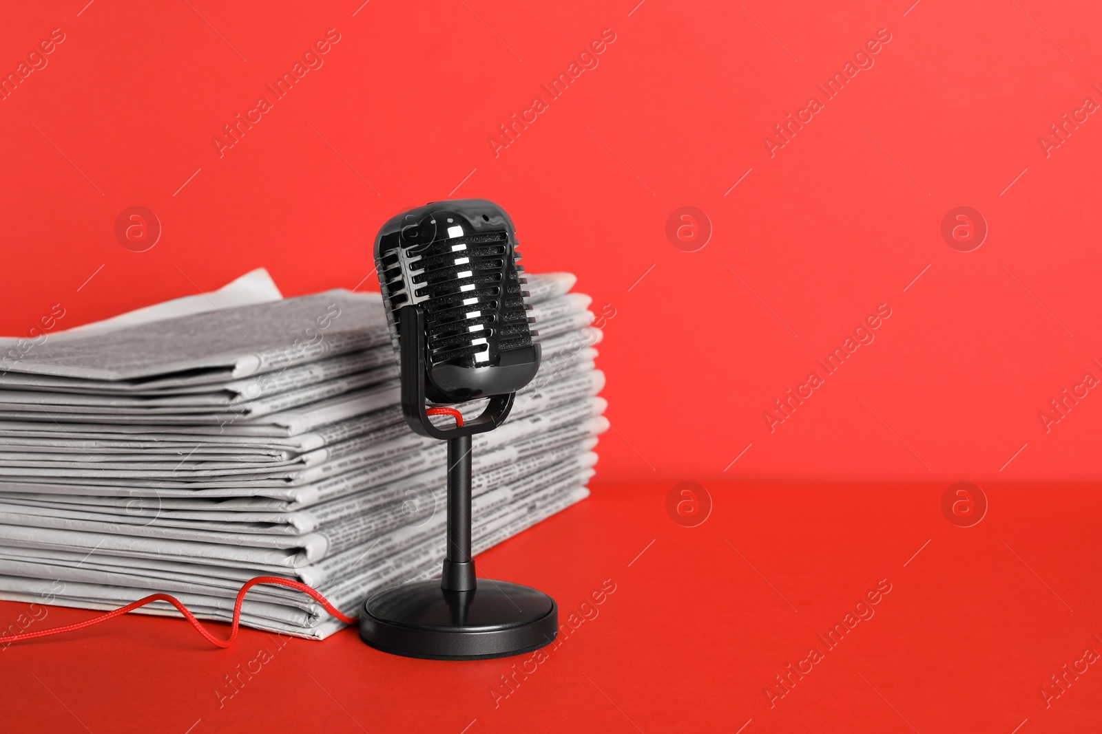 Photo of Newspapers and vintage microphone on red background, space for text. Journalist's work