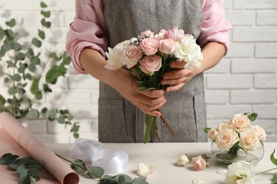 Photo of Florist creating beautiful bouquet at white table indoors, closeup