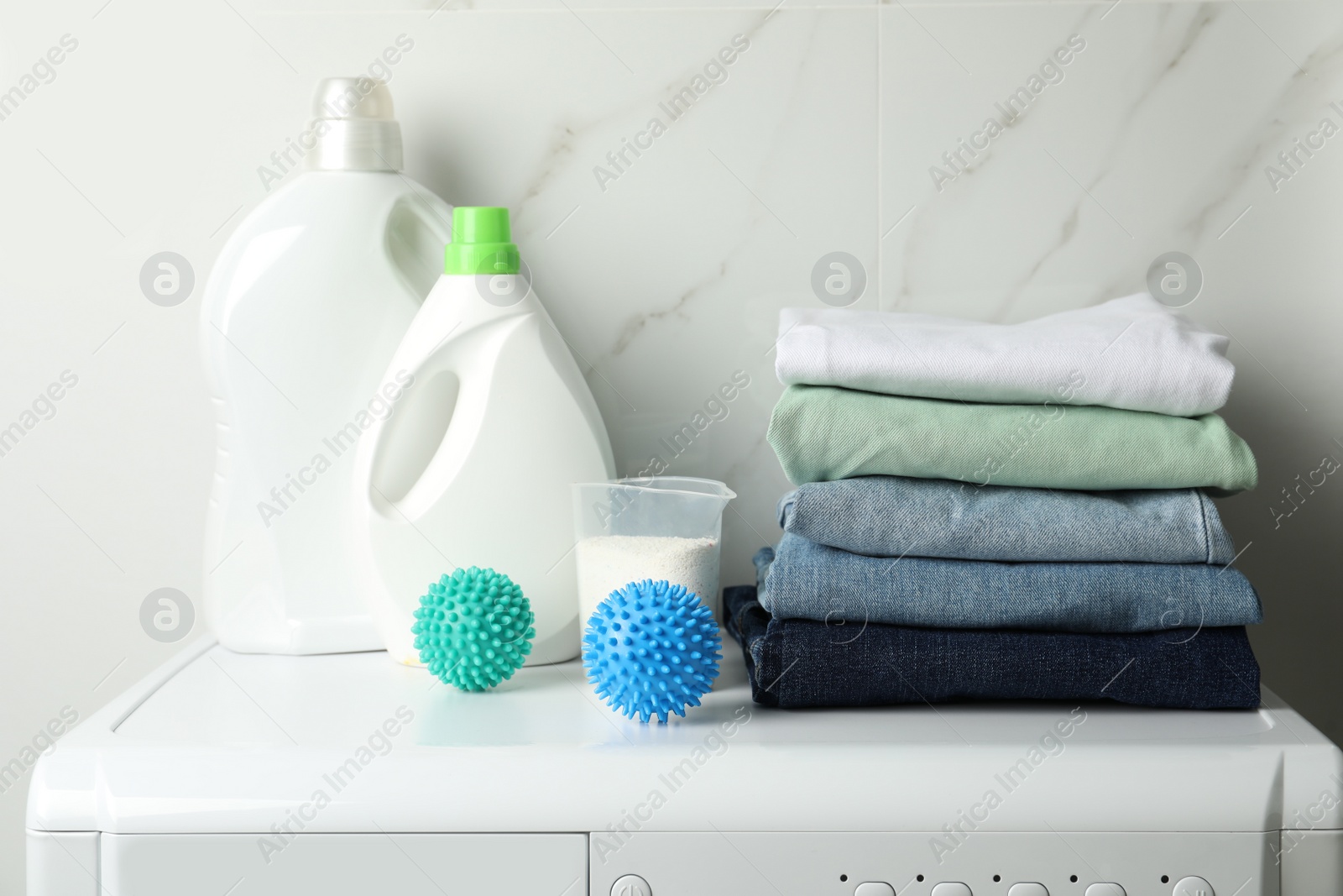 Photo of Dryer balls, stacked clean clothes and detergents on washing machine