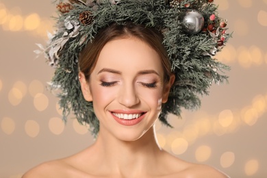 Photo of Beautiful young woman wearing Christmas wreath against blurred festive lights, closeup