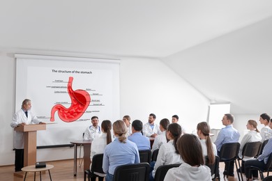 Lecture in gastroenterology. Conference room full of professors and doctors. Projection screen with structure of stomach