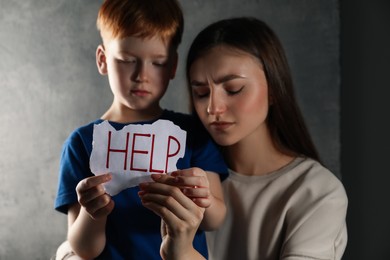 Photo of Scared little boy and mother holding piece of paper with word Help against light grey background, focus on hands. Domestic violence concept