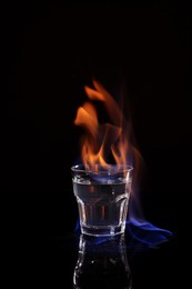 Flaming vodka in shot glass on black background