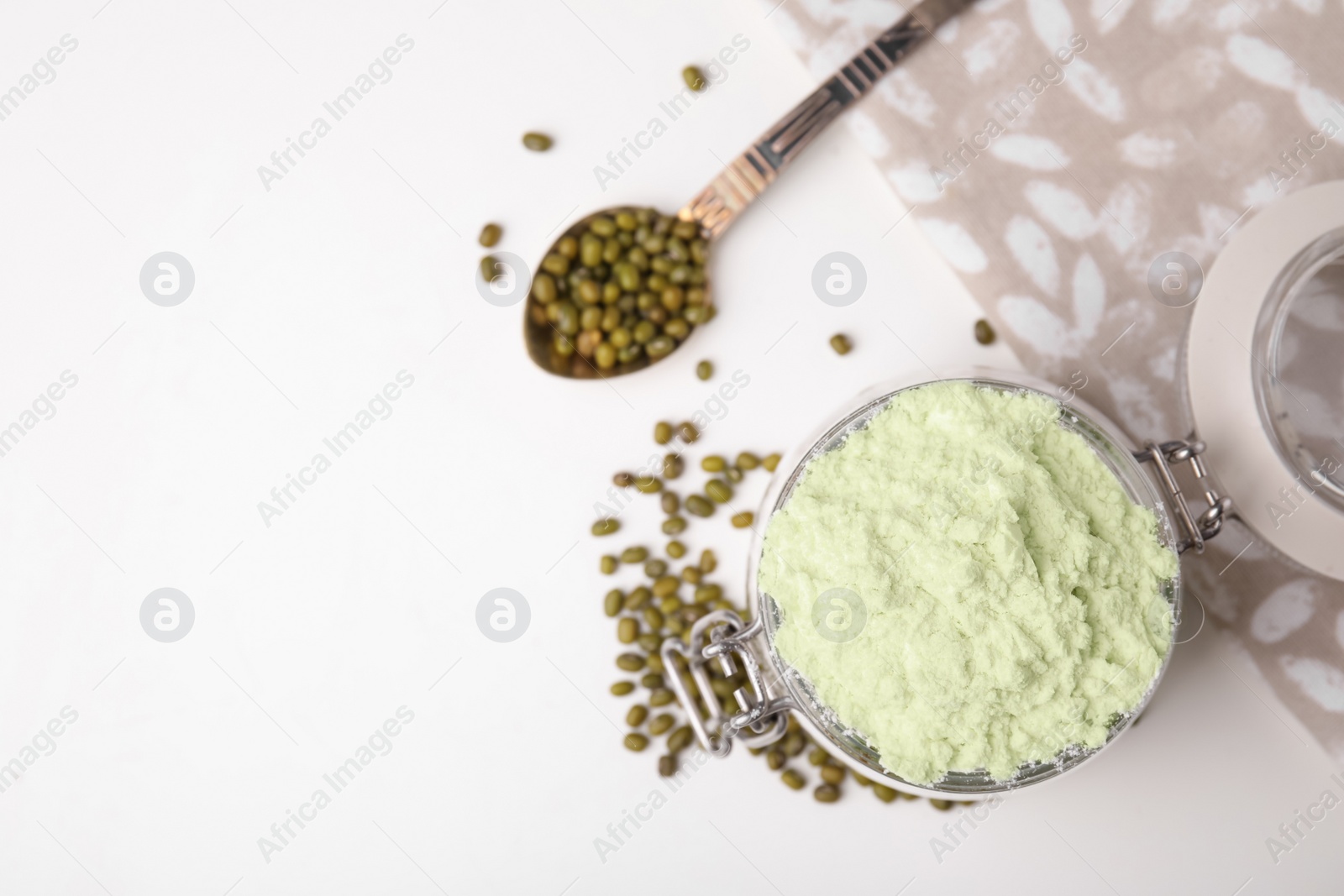 Photo of Glass jar with flour, spoon and mung beans on white table, flat lay. Space for text