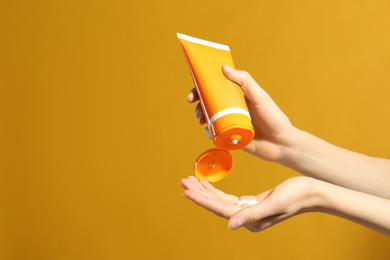 Photo of Woman applying sun protection cream on hand against yellow background, closeup. Space for text