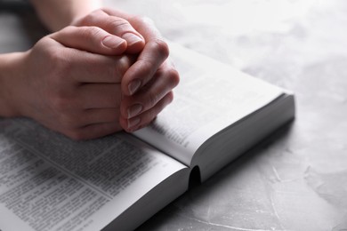 Photo of Religion. Christian woman praying over Bible at gray textured table, closeup