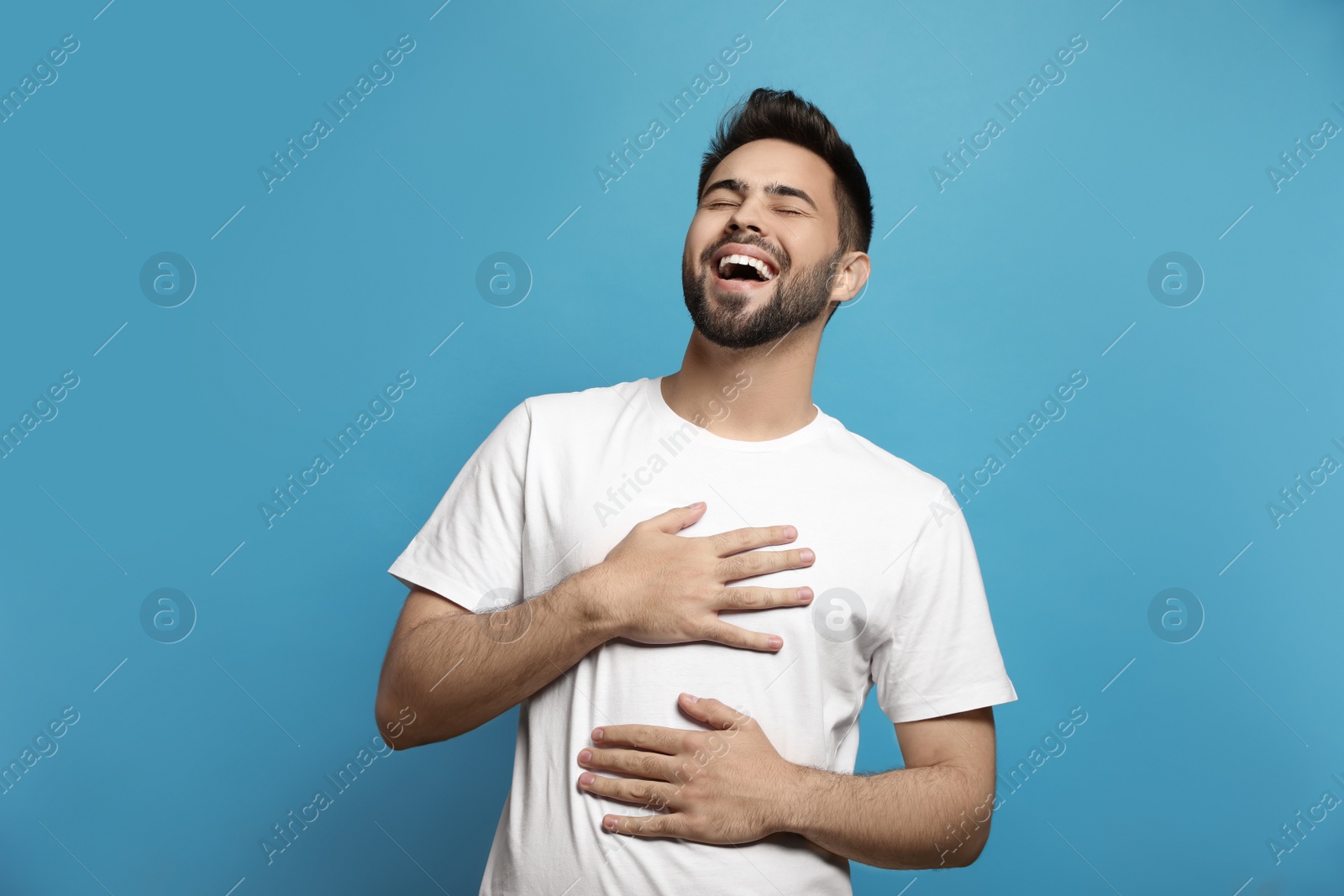 Photo of Young man laughing on light blue background. Funny joke