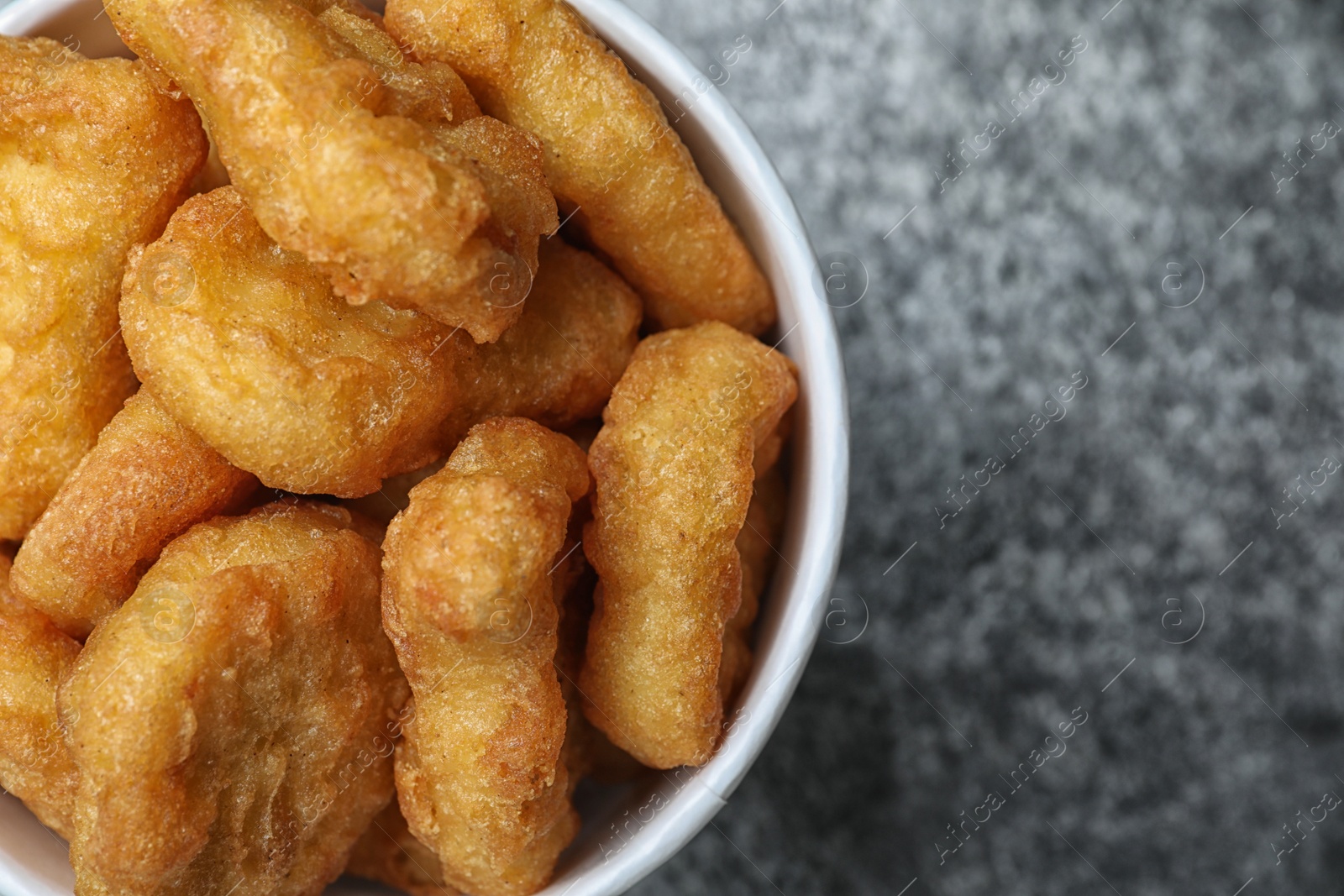 Photo of Bucket with tasty chicken nuggets on grey table, top view