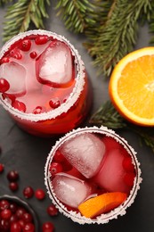 Photo of Tasty cranberry cocktail with ice cubes in glasses on dark gray table, flat lay