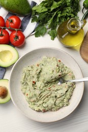 Photo of Delicious guacamole in bowl and ingredients on white wooden table, flat lay