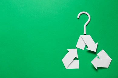 Photo of Recycling symbol in shape of hanger on green background, top view. Space for text