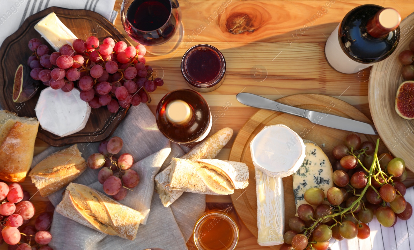 Photo of Red wine and snacks served for picnic on wooden table outdoors, flat lay