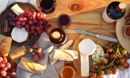 Red wine and snacks served for picnic on wooden table outdoors, flat lay