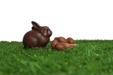 Chocolate bunny and eggs on green grass against white background, space for text. Easter celebration