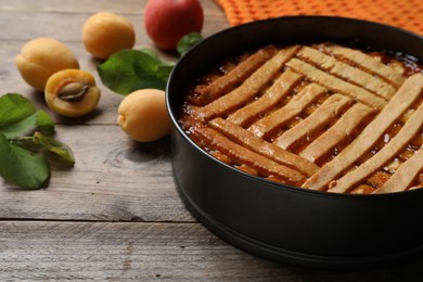 Delicious apricot pie in baking dish and fresh fruits on wooden table, closeup